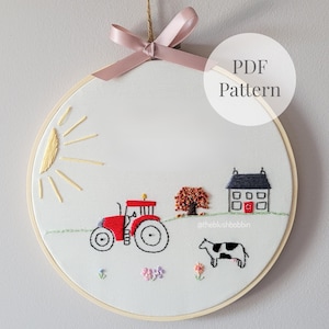 Puede incluir: Un bastidor de bordado circular con tela blanca que muestra una escena de granja cosida a mano con un tractor rojo, una casa, una vaca, un sol y un árbol. Un lazo rosa está atado en la parte superior. El texto PDF Pattern es visible.