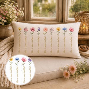 Puede incluir: Un cojín rectangular de color blanco roto con una fila de nueve ilustraciones florales al estilo acuarela. Cada tallo de flor va acompañado del texto en cursiva "this is some bullshit" impreso en tono dorado a lo largo del tallo.
