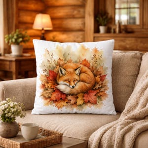 Peut inclure: Un coussin carré décoré d'une illustration à l'aquarelle représentant un renard roux recroquevillé et endormi au milieu d'un tas de feuilles d'automne aux tons orange, rouge et jaune, sur un fond blanc net de la housse de coussin.