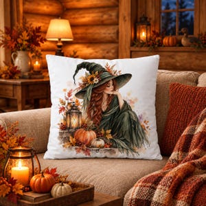 May include: A square white throw pillow featuring a watercolor illustration of a person with long red hair wearing a wide-brimmed green witch hat. The design includes a glowing lantern, orange pumpkins, and autumn leaves in shades of red and gold.
