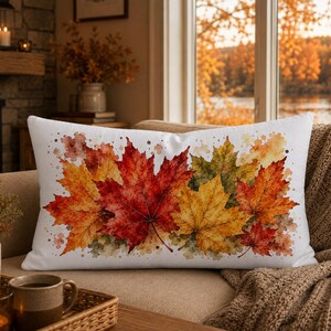 May include: A rectangular white throw pillow featuring a watercolour illustration of autumn maple leaves in shades of vibrant red, burnt orange, and golden yellow, accented with subtle brown and green paint splatters across the fabric surface.