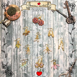 Può includere: Assortimento di orecchini fatti a mano per bambole. Gli orecchini sono realizzati con vari materiali, tra cui oro, perline e tessuto. Gli orecchini sono esposti su uno sfondo di legno con il testo "Snow White Fashion for dolls made in Italy".