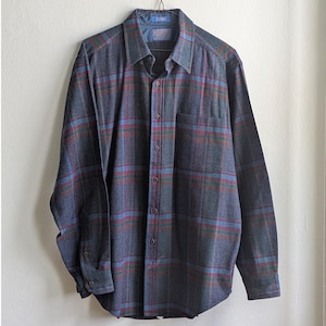 May include: A long-sleeved, button-down shirt in a plaid pattern of blue, red, and green on a gray background. The shirt has a chest pocket and is hanging on a black hanger. The collar is a darker shade of gray.