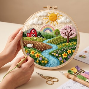Può includere: Un telaio da ricamo circolare contenente una scena paesaggistica strutturata con un fienile rosso, un fiume blu sinuoso, un sole giallo, un arcobaleno, un albero in fiore e una pecora bianca. La scena presenta colline verdi e fiori colorati.