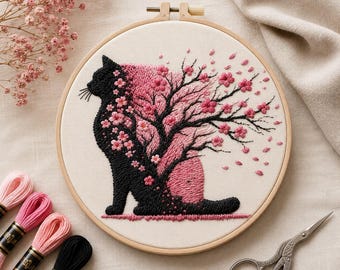 May include: A circular wooden embroidery hoop containing a fabric panel with a stitched design of a black cat silhouette. The cat's body transitions into a black tree with pink cherry blossom flowers, with petals scattering across the cream fabric.
