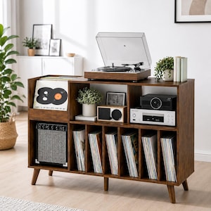 May include: A dark wood media console with tapered legs, featuring a top surface for a turntable, a dedicated vertical slot for vinyl records, and multiple open shelves housing a small amplifier, a speaker, and a collection of vinyl records.