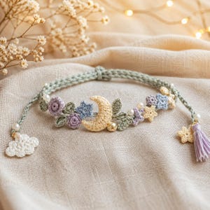 Könnte beinhalten: Gehäkeltes Stirnband mit Mond, Sternen und Blumen in Pastellfarben. Das hellgrüne Band hat eine Quaste und einen Wolkenanhänger. Das Design beinhaltet Perlen und zeigt eine zarte, handgefertigte Ästhetik. Ein einzigartiges Accessoire.