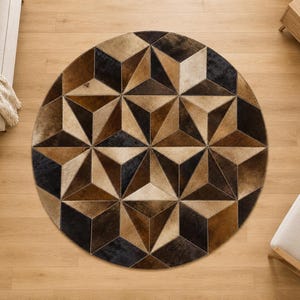 May include: A circular area rug featuring a geometric pattern composed of triangular panels in shades of dark brown, tan, and cream. The design creates a three-dimensional cube effect across the surface, with stitched seams connecting each individual piece of material.