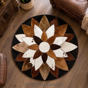 May include: A circular area rug featuring a floral pattern composed of individual cowhide patches in shades of black, white, dark brown, and light brown. The design consists of a central white circle surrounded by multiple layers of petal-shaped pieces.