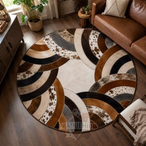 Puede incluir: Una alfombra redonda con un patrón geométrico de arcos concéntricos superpuestos en tonos marrón, negro, crema y gris. El diseño incorpora parches texturizados estilo piel de vaca con acabados moteados y sólidos, centrados en un círculo crema.