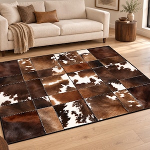 May include: A rectangular area rug constructed from a patchwork of cowhide squares. The rug features a repeating pattern of brown, tan, and white fur patches, each stitched together with visible dark thread along the edges of every square.
