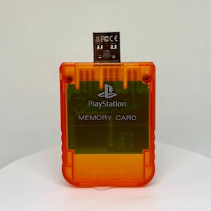 May include: An orange PlayStation memory card with a USB drive inserted. The card has the PlayStation logo and the words "MEMORY CARD" printed on it. The USB drive has the text "32GB" printed on it.
