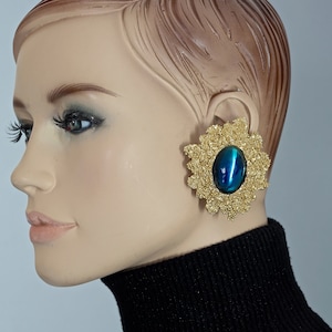 May include: Gold tone clip-on earrings with a large blue iridescent oval stone set in a textured flower design.