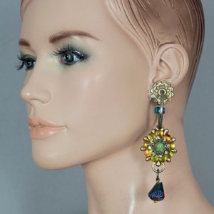 May include: A pair of gold-toned dangle earrings with a green and yellow flower design and a blue and green teardrop-shaped bead.