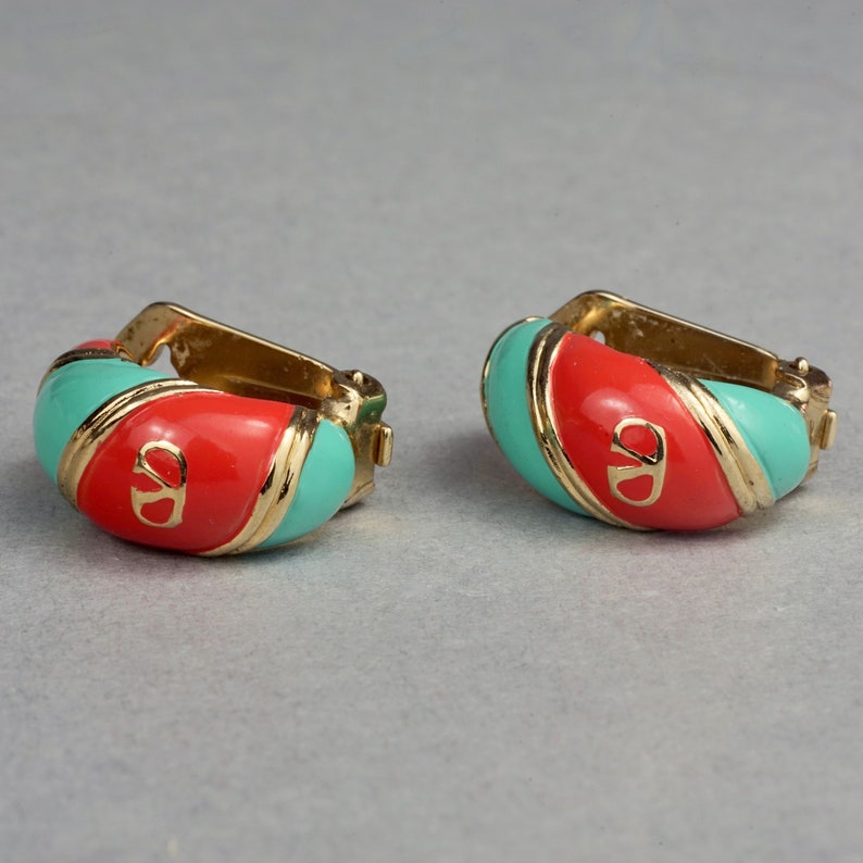 May include: A pair of gold hoop earrings with red and turquoise enamel. The earrings feature a gold logo in the center.