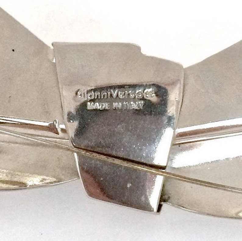 以下が含まれることがあります： 裏側に「Gianni Versace Made in Italy」の文字が刻まれた、銀製の蝶ネクタイの形をしたブローチです。