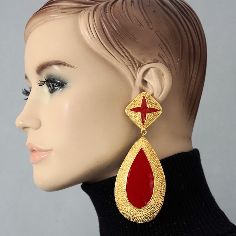 May include: Gold tone dangle earrings with a red enamel teardrop and a red enamel cross on the top.