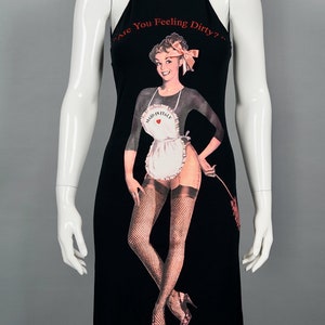 May include: Black halter dress featuring a vintage-style illustration of a woman in an apron and fishnet stockings. The text "Are You Feeling Dirty?" is printed across the top. The dress is displayed on a mannequin.