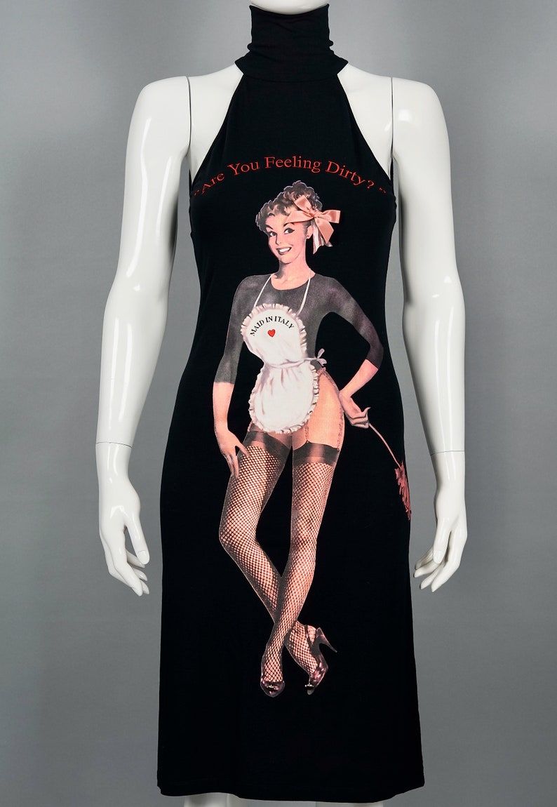May include: Black halter dress featuring a vintage-style illustration of a woman in an apron and fishnet stockings. The text "Are You Feeling Dirty?" is printed across the top. The dress is displayed on a mannequin.