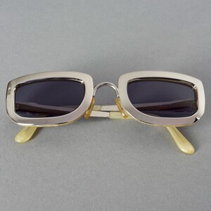 May include: Silver-framed sunglasses with dark lenses and ivory-colored arms.