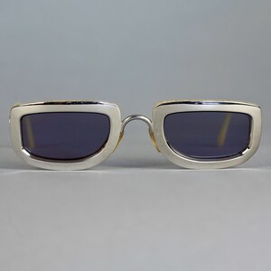 May include: Silver framed sunglasses with dark lenses. The frame has a subtle, textured pattern.