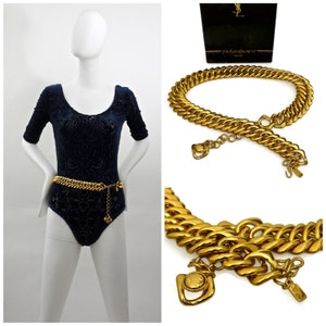 Pode incluir: Um cinto de corrente dourado com um fecho com o logotipo YSL. O cinto é feito de correntes grossas e ligadas e tem um design simples e elegante.