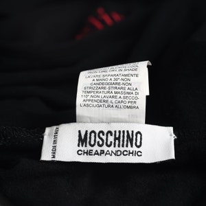 May include: Close-up of a black garment with two white tags. The top tag has washing instructions in Italian. The bottom tag reads "MOSCHINO CHEAPANDCHIC" with "MADE IN ITALY" printed on the left side.
