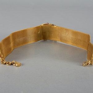 May include: A gold mesh choker necklace with a red and clear stone embellishment. The necklace has a clasp closure.