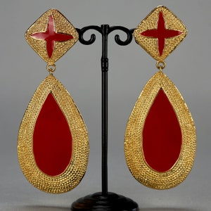May include: A pair of gold tone dangle earrings with red enamel crosses and teardrop shaped drops.