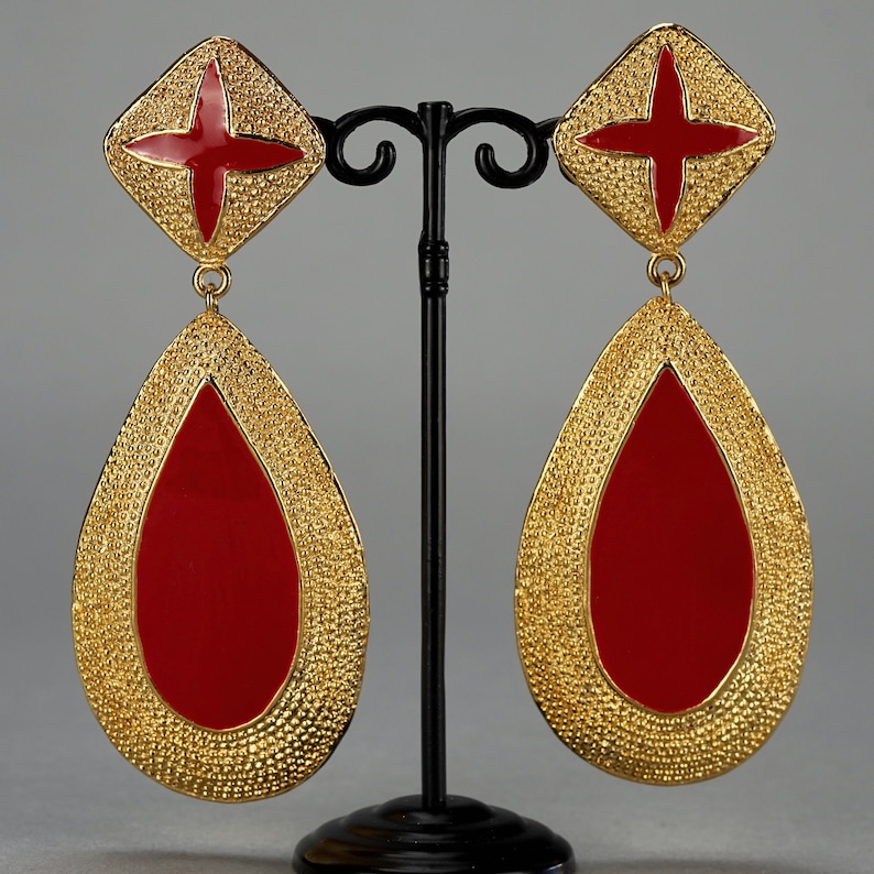 May include: A pair of gold tone dangle earrings with red enamel crosses and teardrop shaped drops.