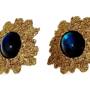 May include: A pair of gold tone earrings with a blue cabochon stone set in each. The earrings have a textured, organic design.