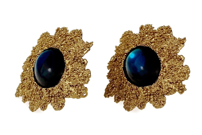 May include: A pair of gold tone earrings with a blue cabochon stone set in each. The earrings have a textured, organic design.