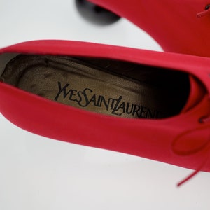 May include: Close-up of the inside of a red leather shoe with the brand name "Yves Saint Laurent" printed on the insole.