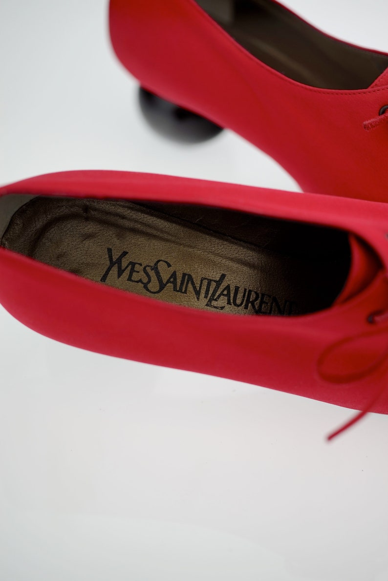 May include: Close-up of the inside of a red leather shoe with the brand name "Yves Saint Laurent" printed on the insole.