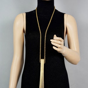 May include: A gold chain necklace with a long, rectangular pendant made of thin, vertical gold bars.