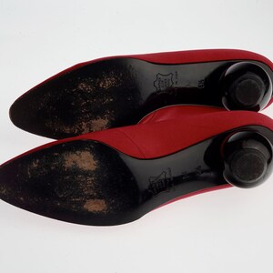 May include: A pair of red satin pumps with black heels and black soles. The heels are rounded and the soles are textured.