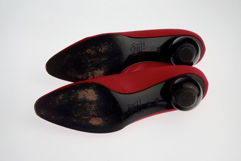 May include: A pair of red satin pumps with black heels and black soles. The heels are rounded and the soles are textured.