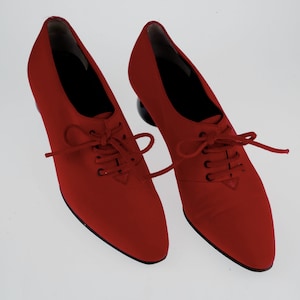 May include: A pair of red lace-up shoes with black laces and a pointed toe. The shoes have a chunky heel.