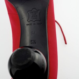 May include: Red leather heels with a black heel and a black ball on the bottom. The heel has the text "Leather Cuir Leder Cuoio Made in Italy" and the size "5 1/2" printed on it.