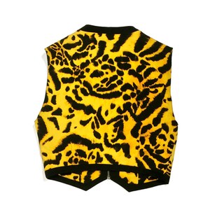 K&ouml;nnte beinhalten: Eine &auml;rmellose Weste mit einem gelben und schwarzen Leopardenmuster. Die Weste hat einen schwarzen Rei&szlig;verschluss und einen spitzen Saum.
