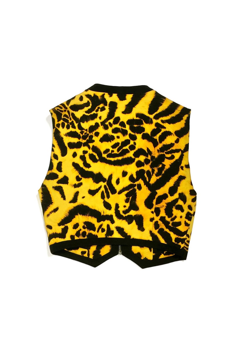 K&ouml;nnte beinhalten: Eine &auml;rmellose Weste mit einem gelben und schwarzen Leopardenmuster. Die Weste hat einen schwarzen Rei&szlig;verschluss und einen spitzen Saum.
