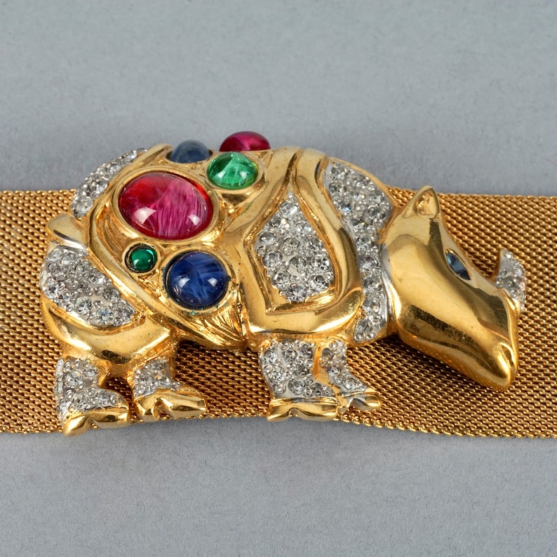 May include: A gold-tone rhinoceros brooch with rhinestones and colorful stones. The brooch is attached to a gold mesh belt.