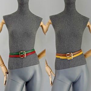 Pode incluir: Dois manequins vestindo cintos de cores diferentes. O cinto do manequim da esquerda &eacute; vermelho, verde e marrom com uma fivela dourada. O cinto do manequim da direita &eacute; amarelo, marrom e laranja com uma fivela dourada.