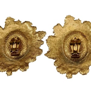 May include: A pair of gold-tone clip-on earrings with a textured, flower-shaped design.