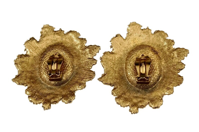 May include: A pair of gold-tone clip-on earrings with a textured, flower-shaped design.