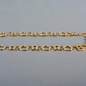 May include: A gold-tone necklace with a repeating pattern of the letter "O" and the letter "R".