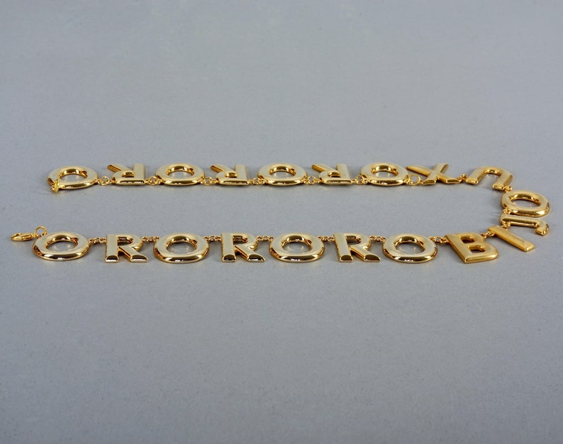 May include: A gold-tone necklace with a repeating pattern of the letter "O" and the letter "R".