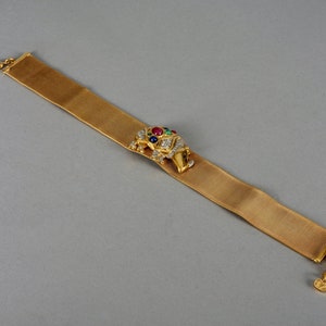 May include: A gold mesh bracelet with a jeweled elephant charm. The elephant is decorated with clear, red, green, and blue gemstones.