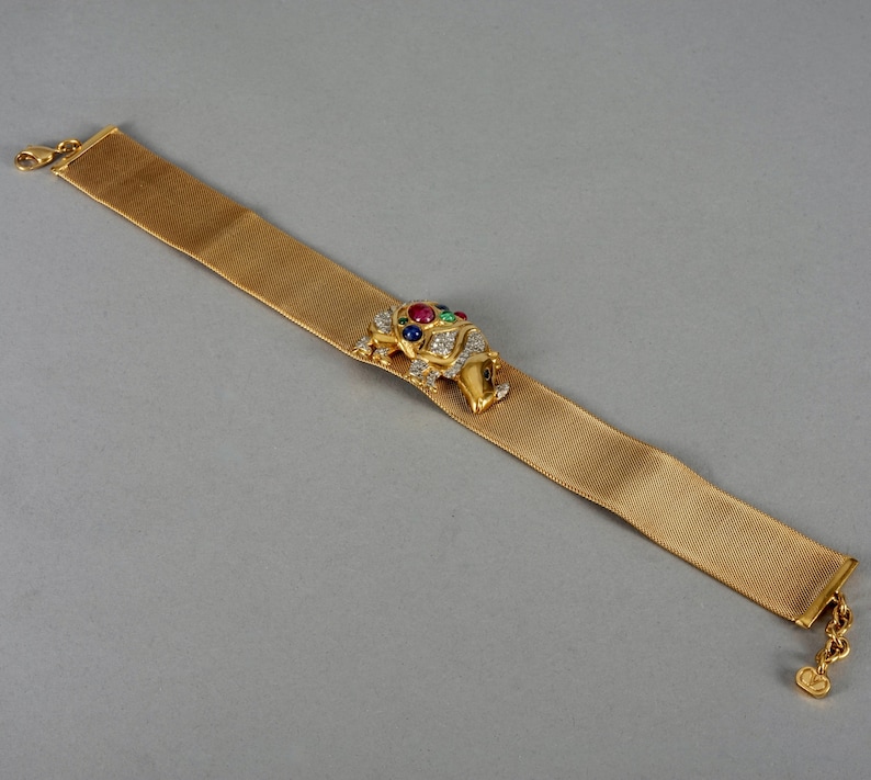 May include: A gold mesh bracelet with a jeweled elephant charm. The elephant is decorated with clear, red, green, and blue gemstones.