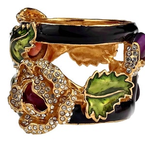 Puede incluir: Anillo de tono dorado con una banda de esmalte negro y un dise&ntilde;o floral tridimensional. La flor est&aacute; adornada con diamantes de imitaci&oacute;n transparentes y tiene un centro rojo y morado. El anillo tambi&eacute;n presenta hojas de esmalte verde.